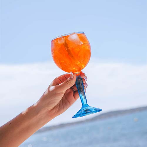 Verre de cocktail Spritz au Prosecco, garni d'orange et de glaçons, tenu face à la mer Méditerranée chez Gaetano Plage à Hyères